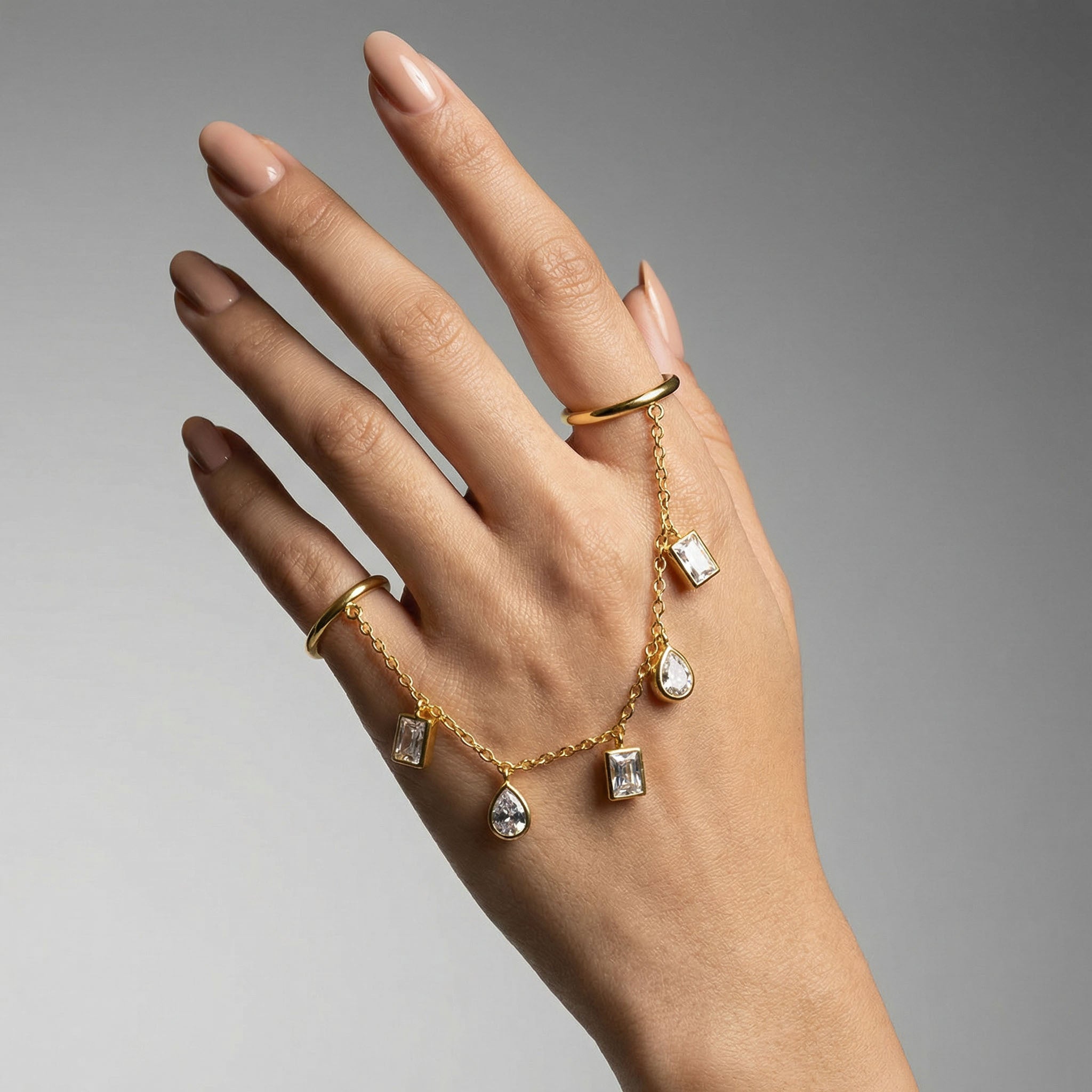 Hand wearing a gold ring with diamond-shaped pendants on a gray background