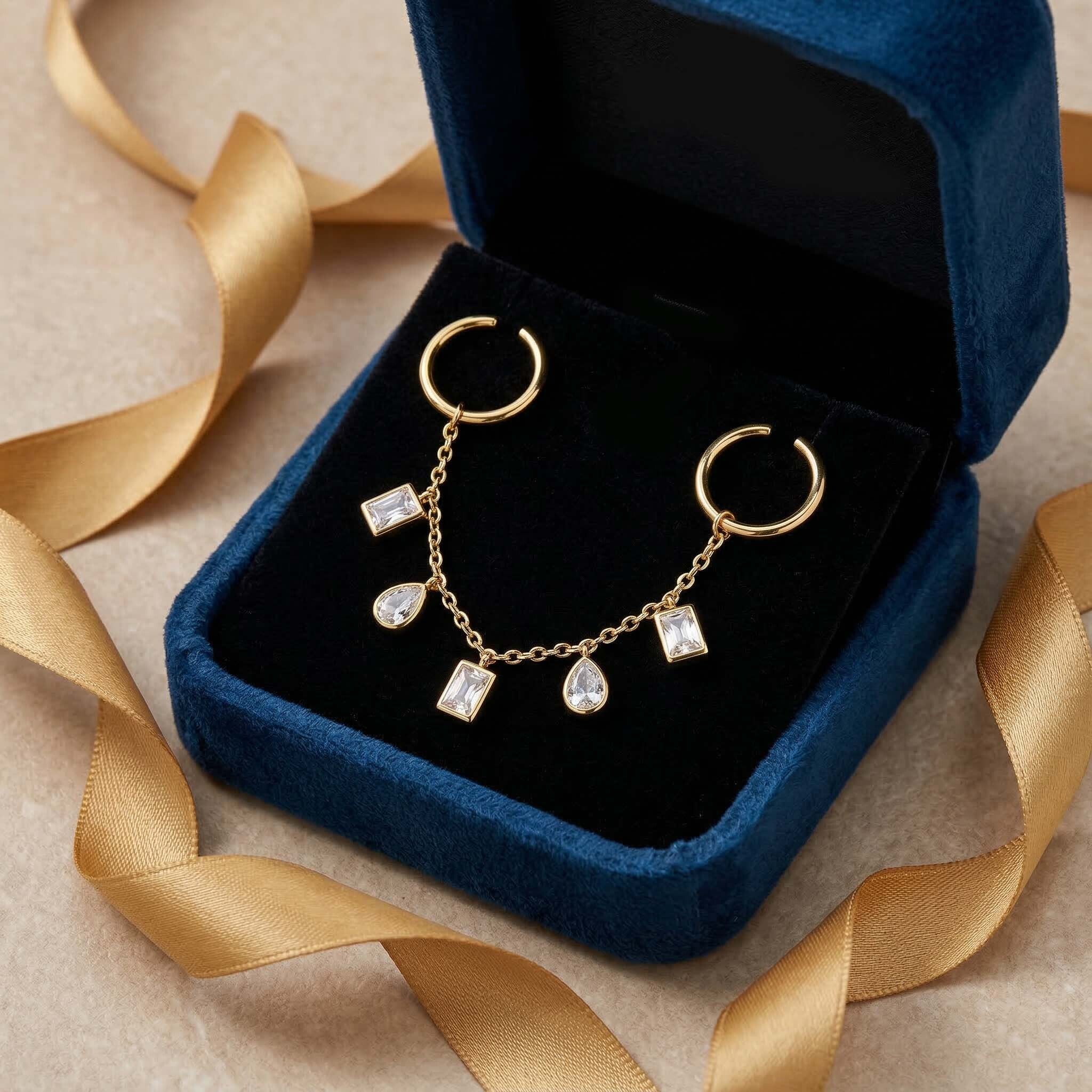 Gold rigns with gemstones in a blue jewelry box on a beige surface with gold ribbons.