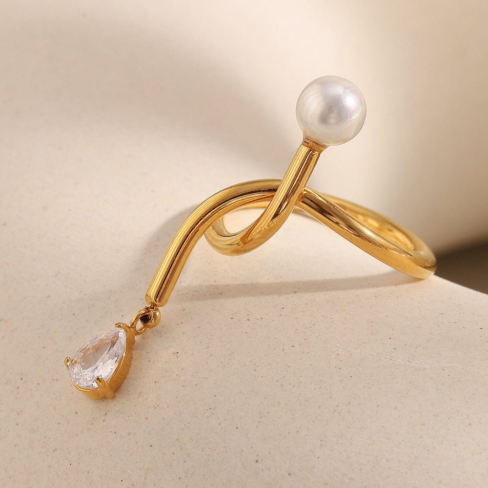 Gold ring with a pearl and teardrop-shaped gemstone on a beige background