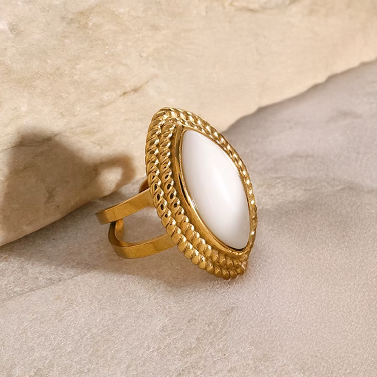 Gold ring with a white stone on a beige stone surface
