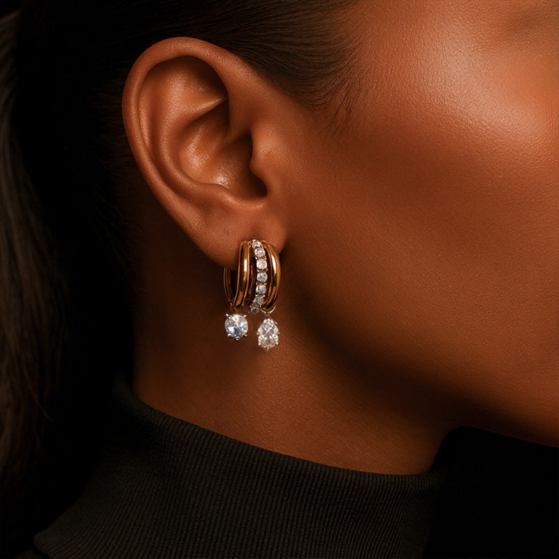 Close-up of an ear wearing a pair of gold hoop earrings with clear stones.