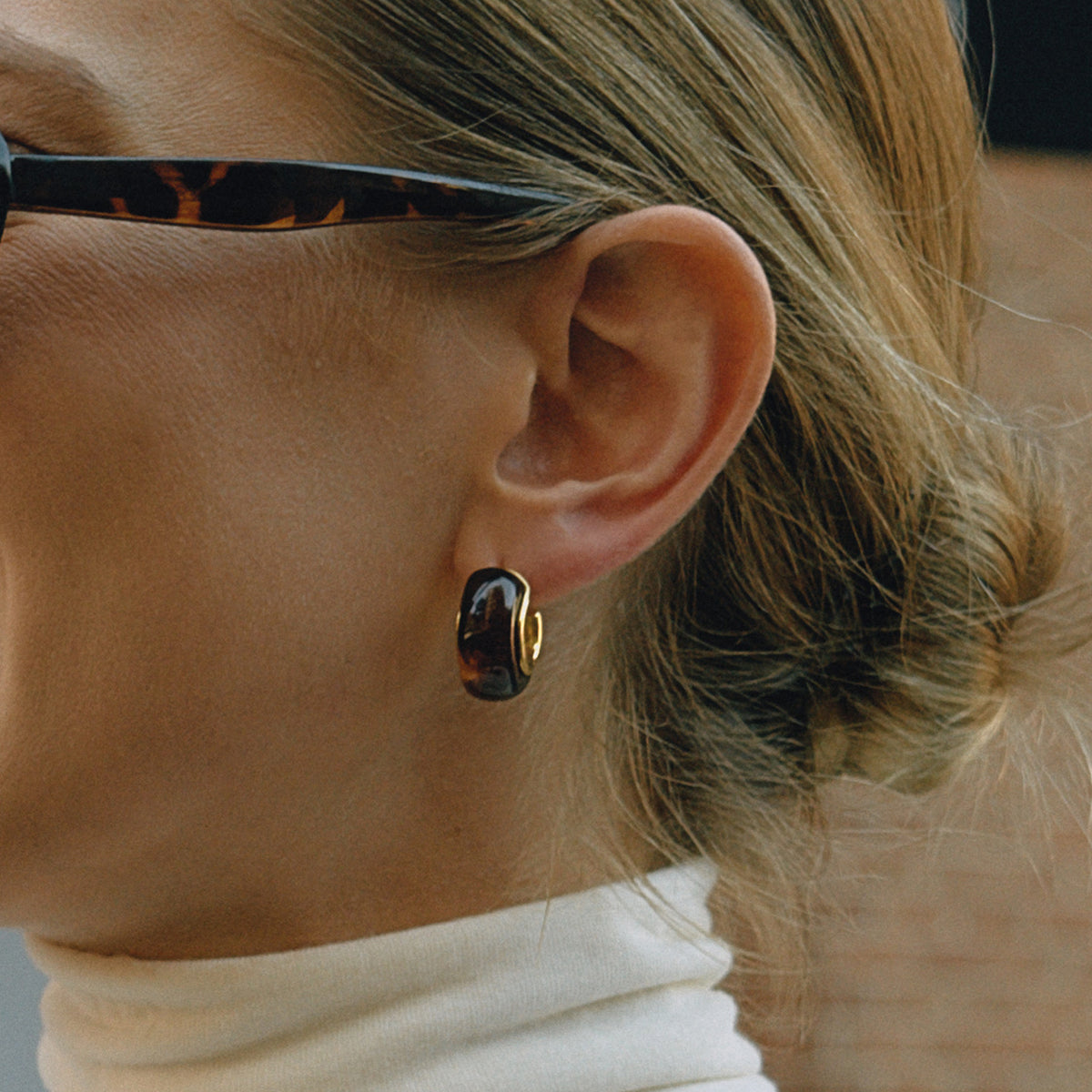 Close-up of an ear wearing a black earring with a gold accent.