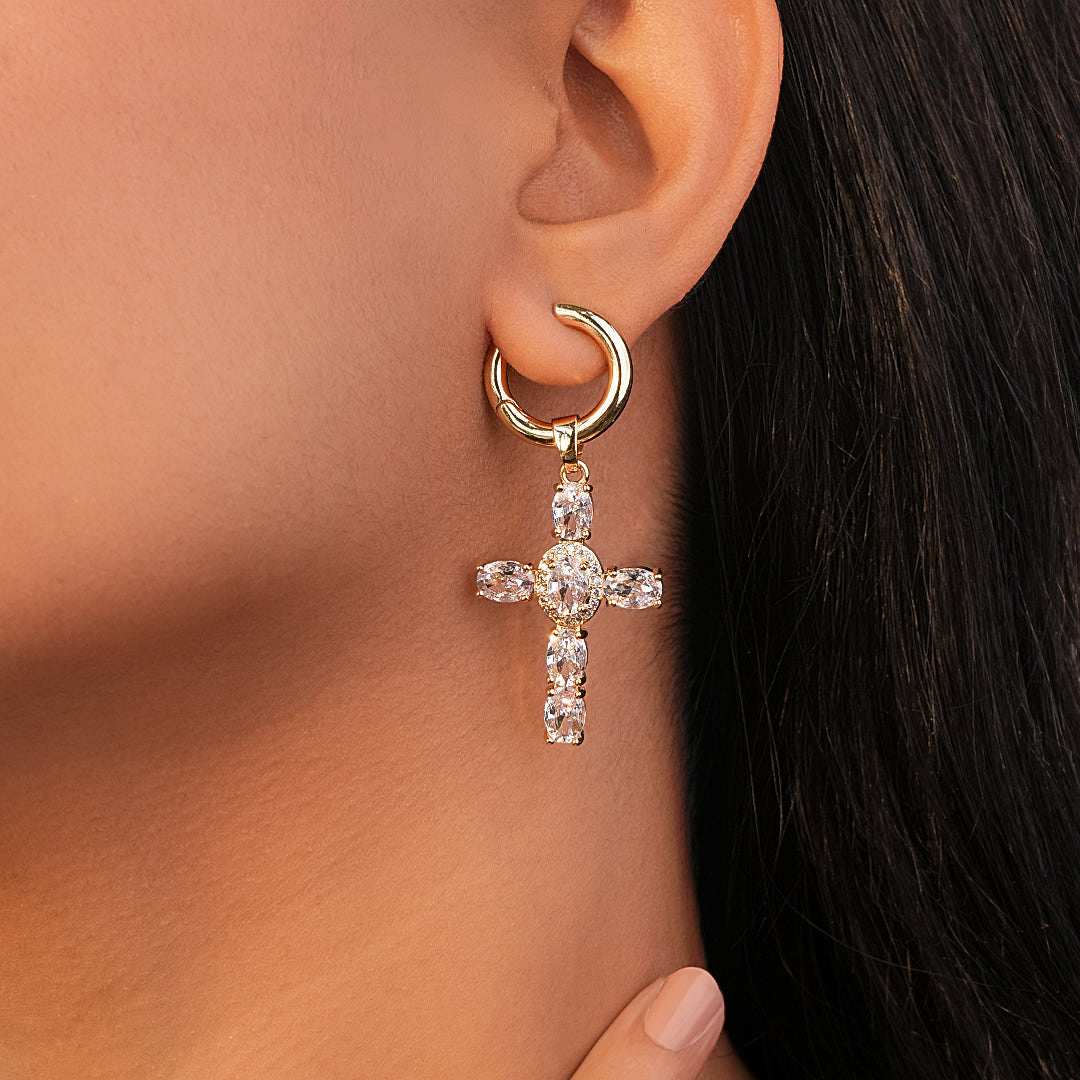 Gold earrings for women with a cross pendant worn by a person