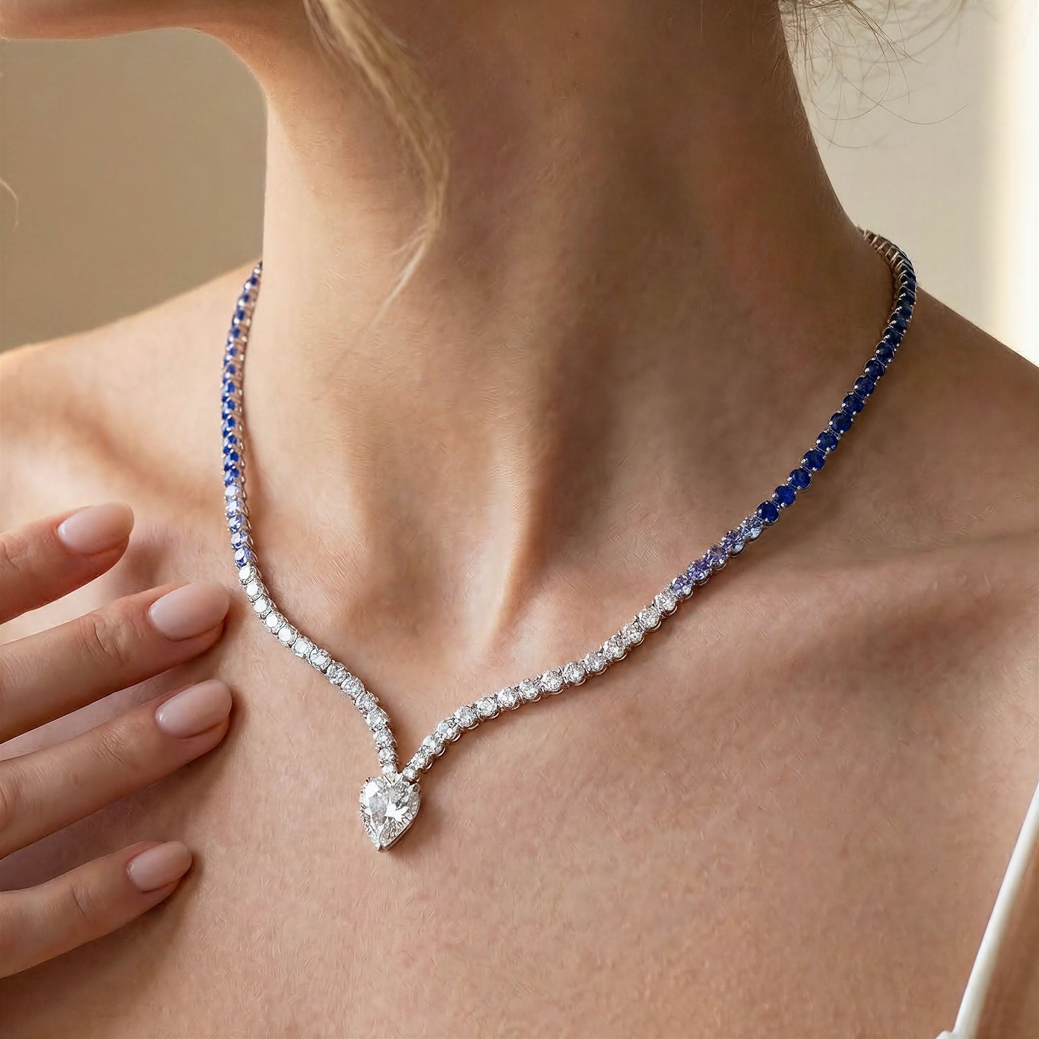 Close-up of a woman wearing a diamond necklace with a blue gemstone on a neutral background