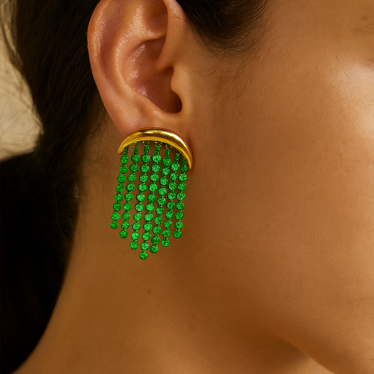Gold earrings for women with green gemstones worn by a person