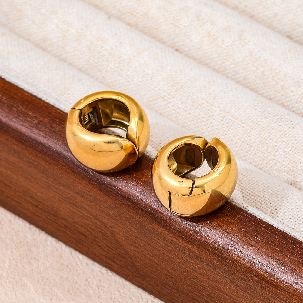 Gold hoop earrings for women on a wooden stand with a beige fabric background