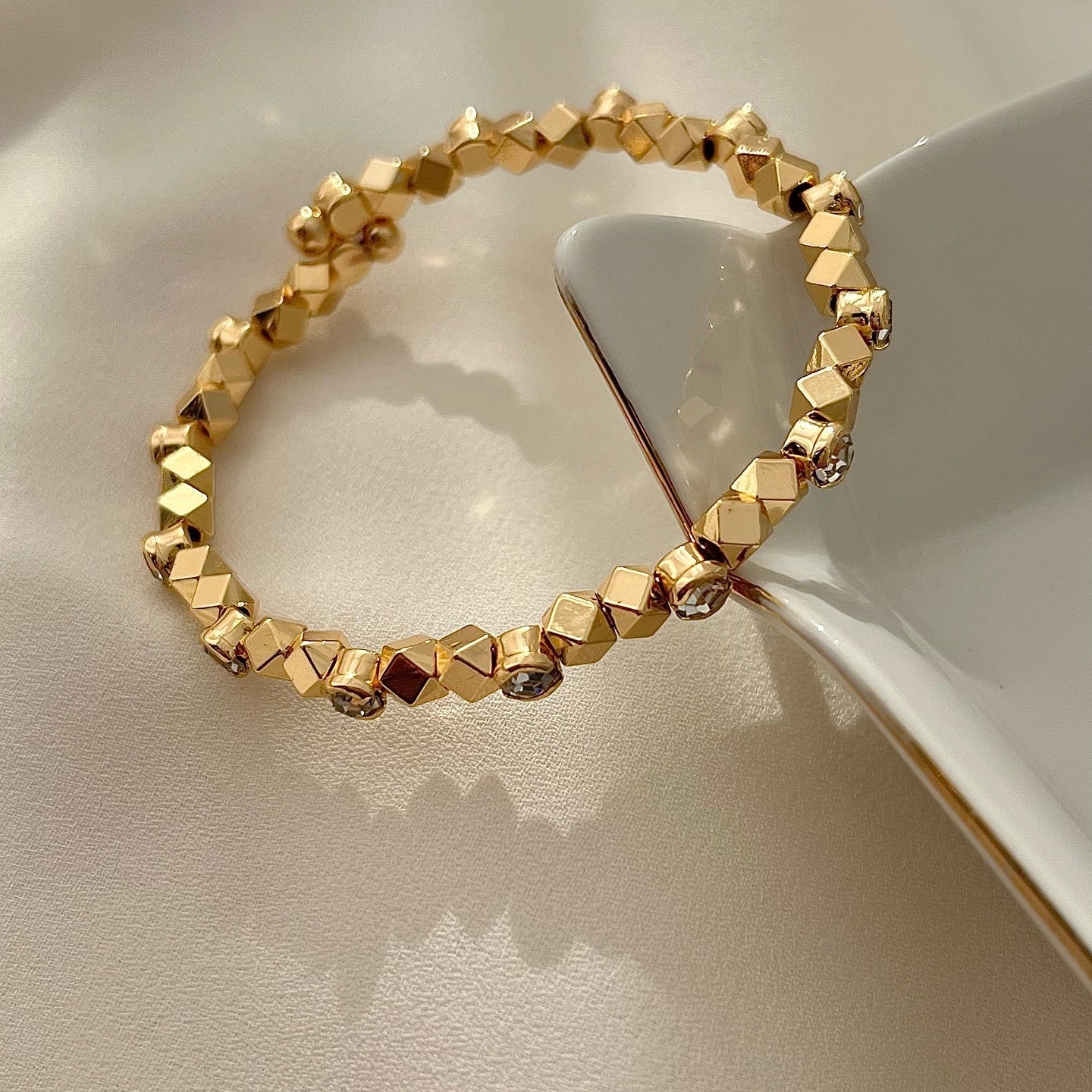 Gold bracelet with geometric beads on a beige surface