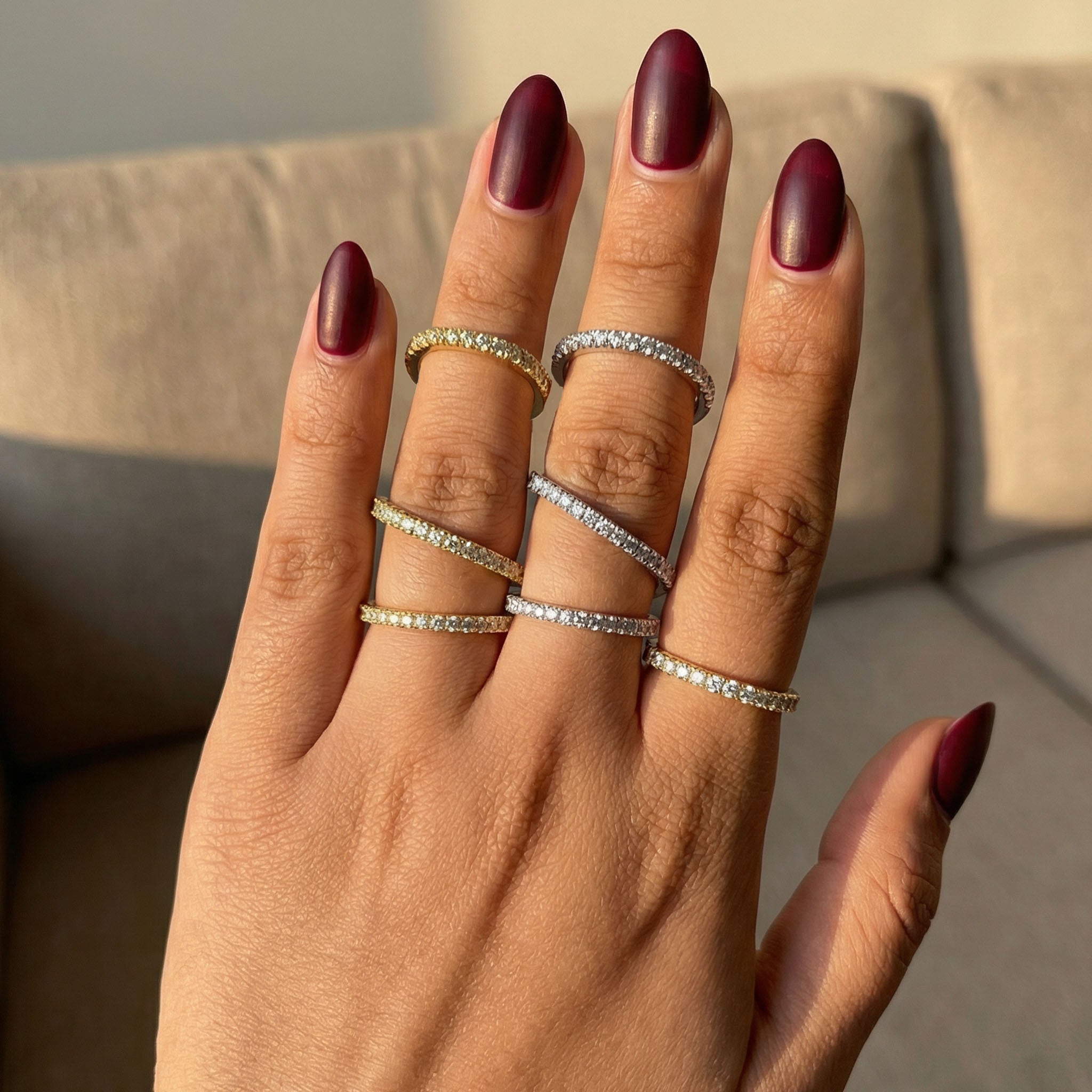 Hand with multiple rings and dark red nail polish on a neutral background