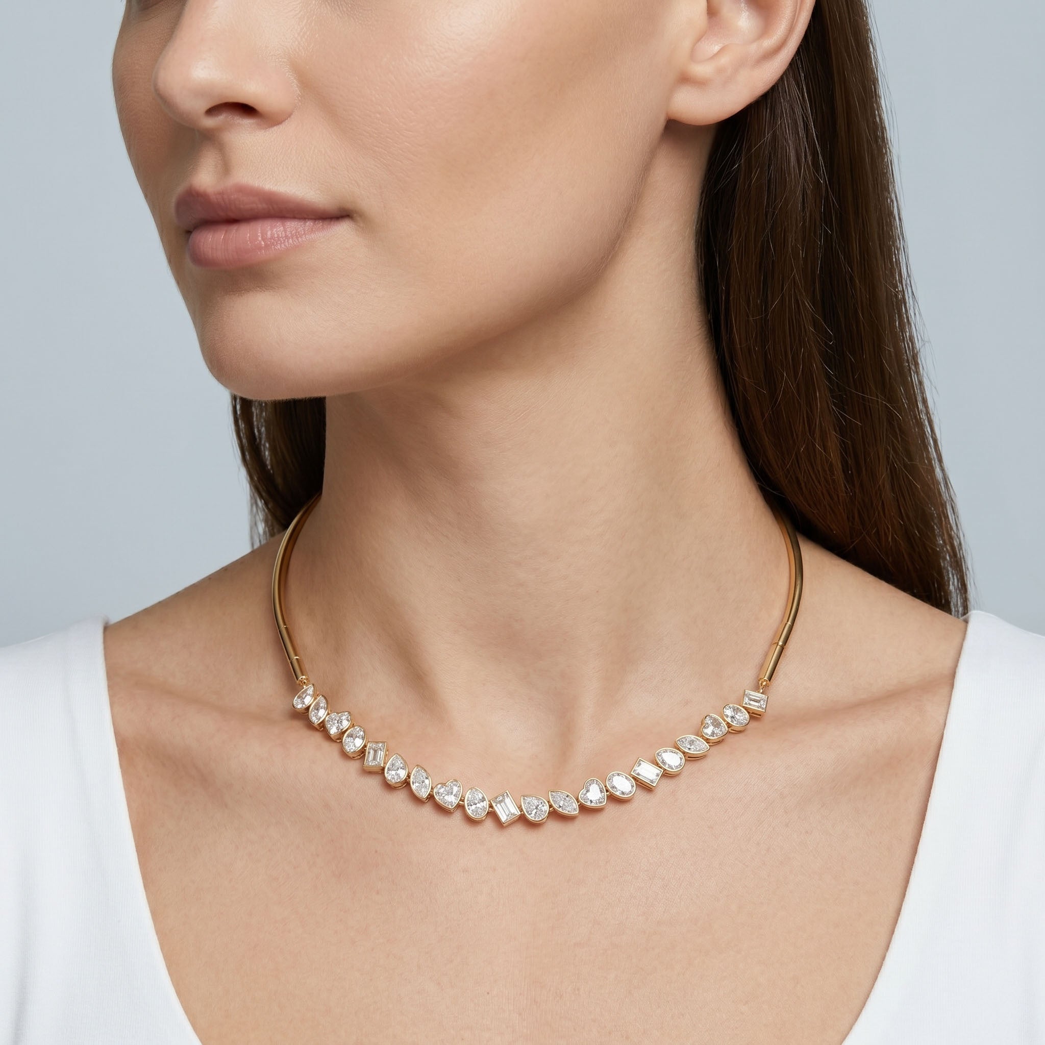 Close-up of a woman wearing a gold necklace with clear stones on a neutral background