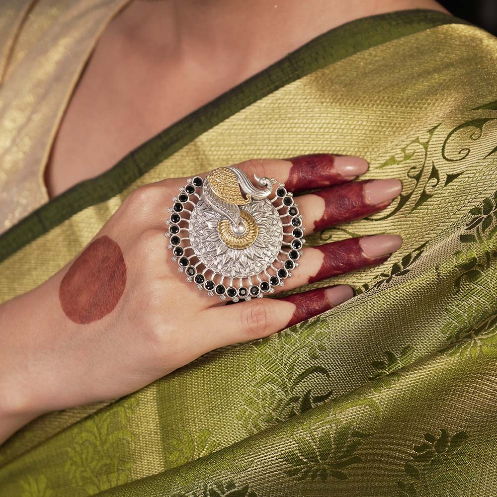 Hand wearing a silver and gold ring with a green saree in the background