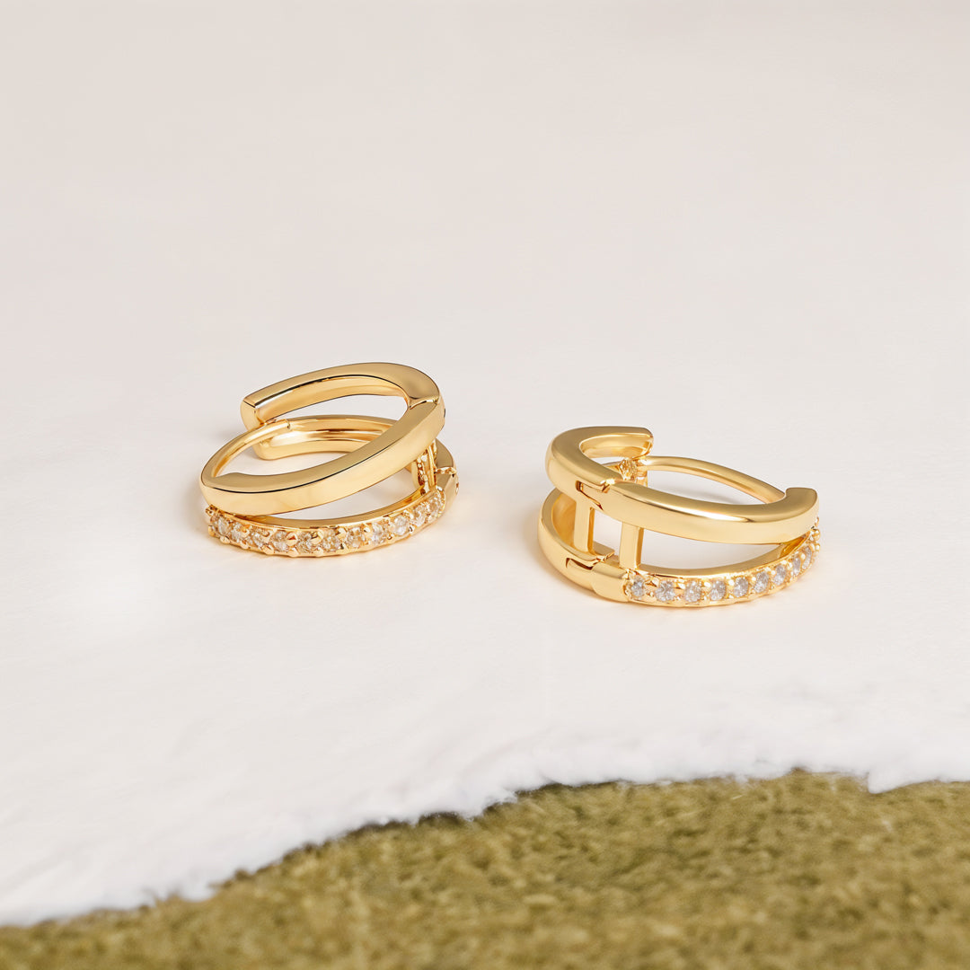 Gold hoop earrings with embedded stones on a textured surface