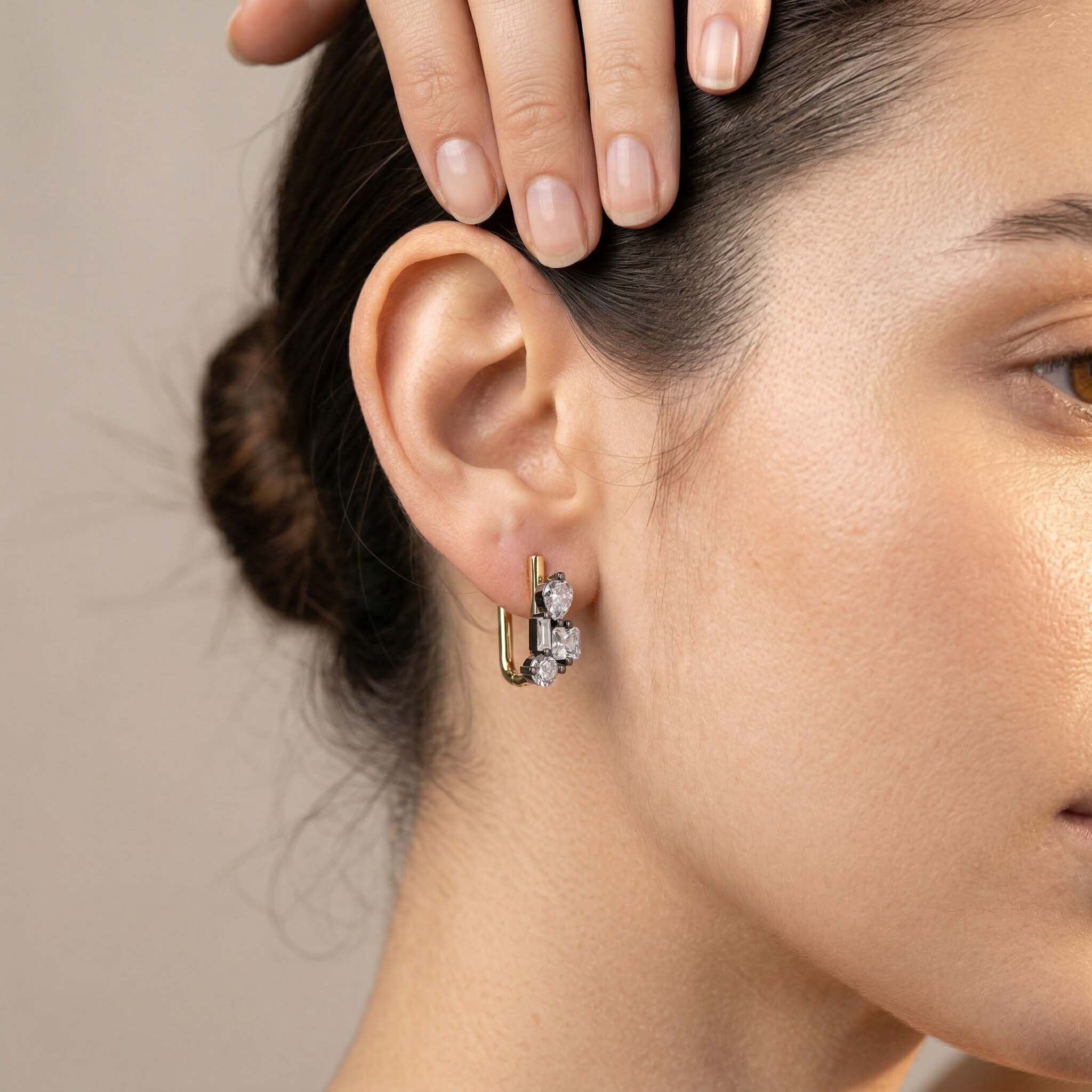 Close-up of a person wearing a gold earring with clear stones.