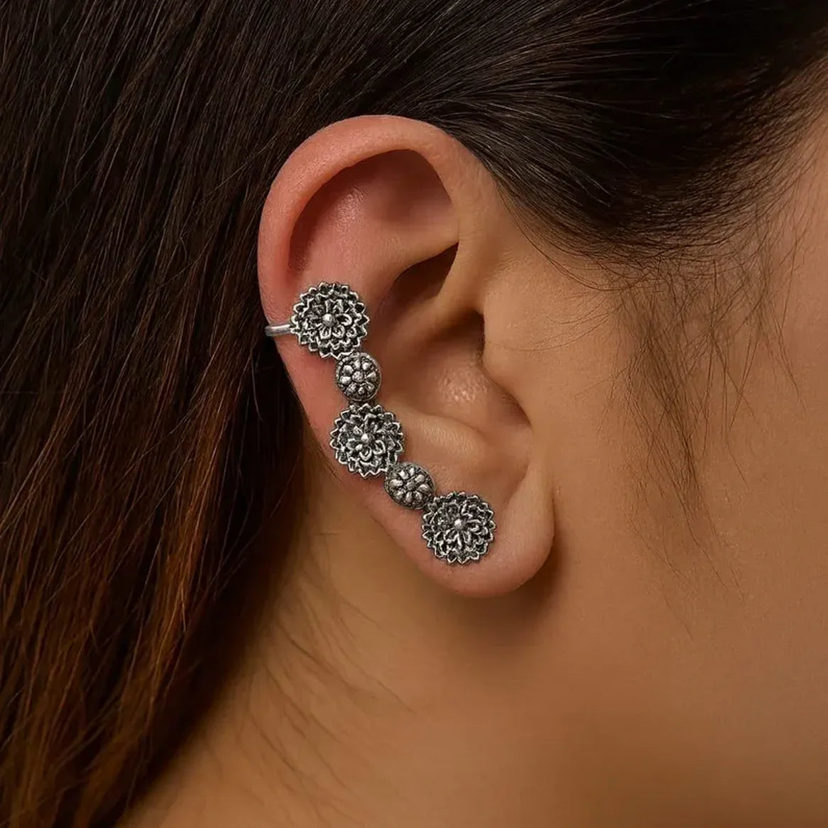 Close-up of an ear wearing a silver floral earring for women with a blurred background