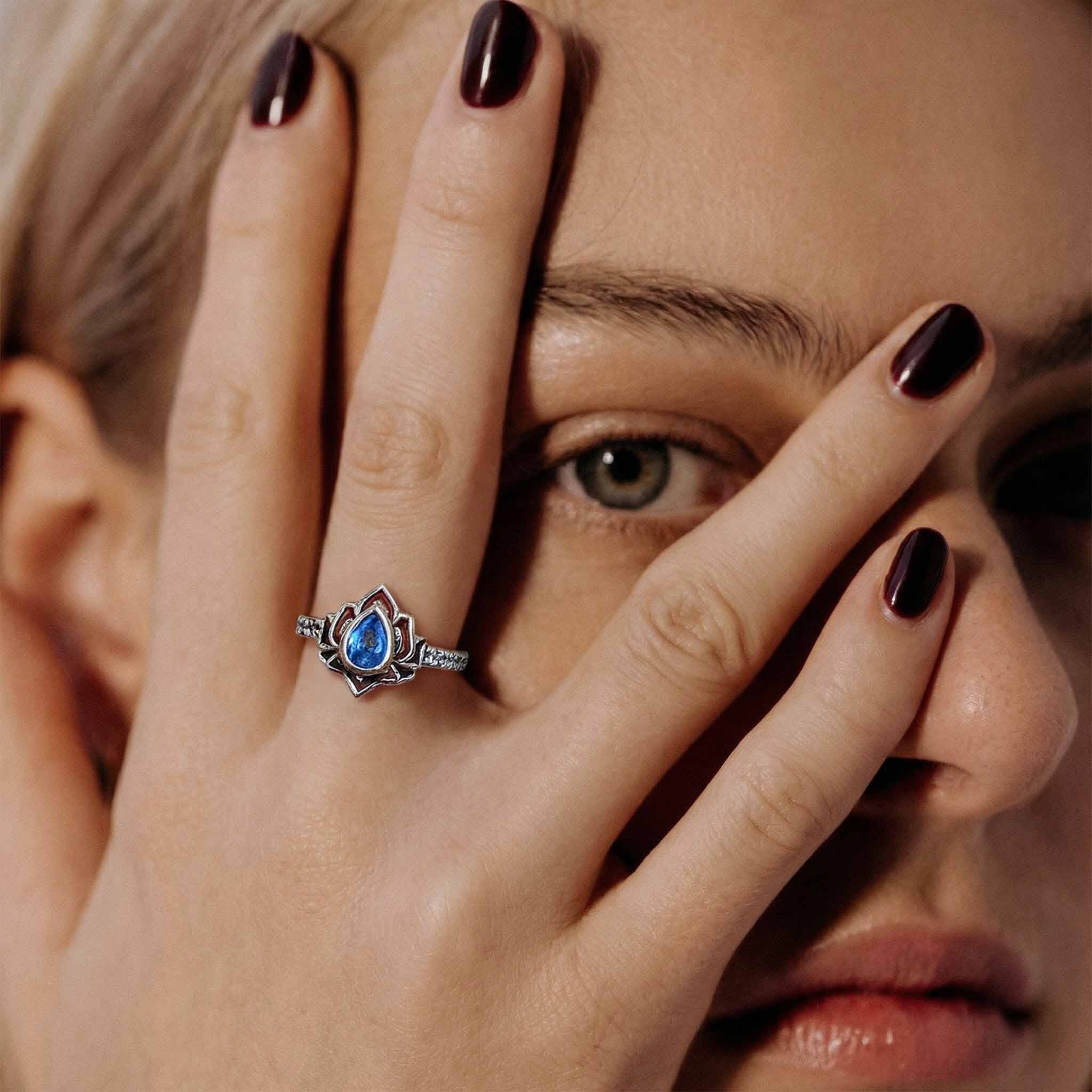 Close-up of a woman's hand with a ring featuring a blue gemstone, covering her face.