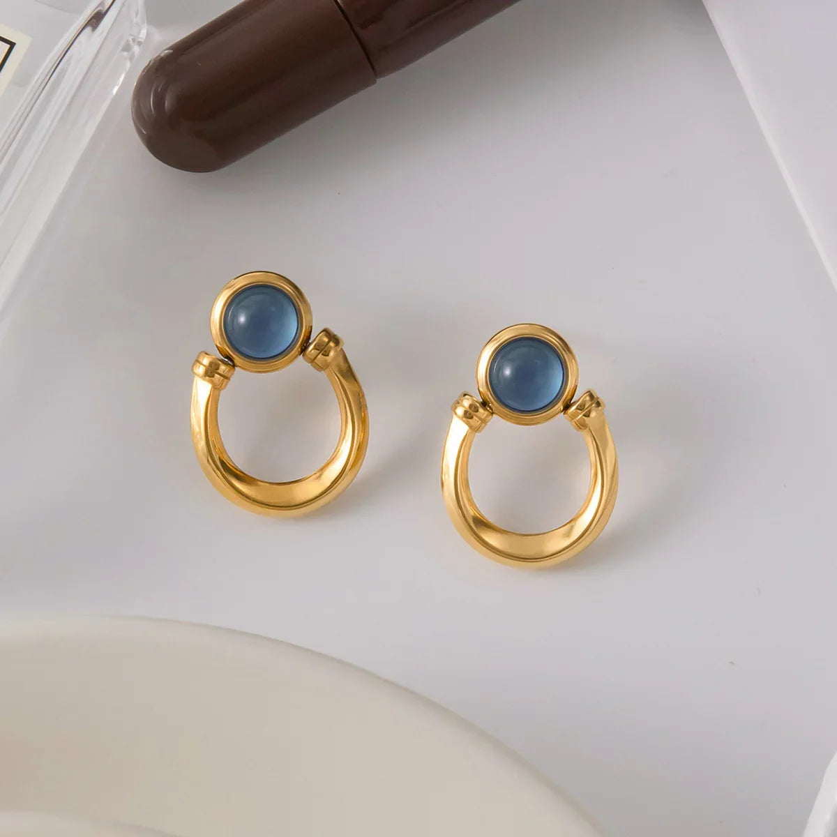 Gold hoop earrings for women with blue gemstones on a white surface