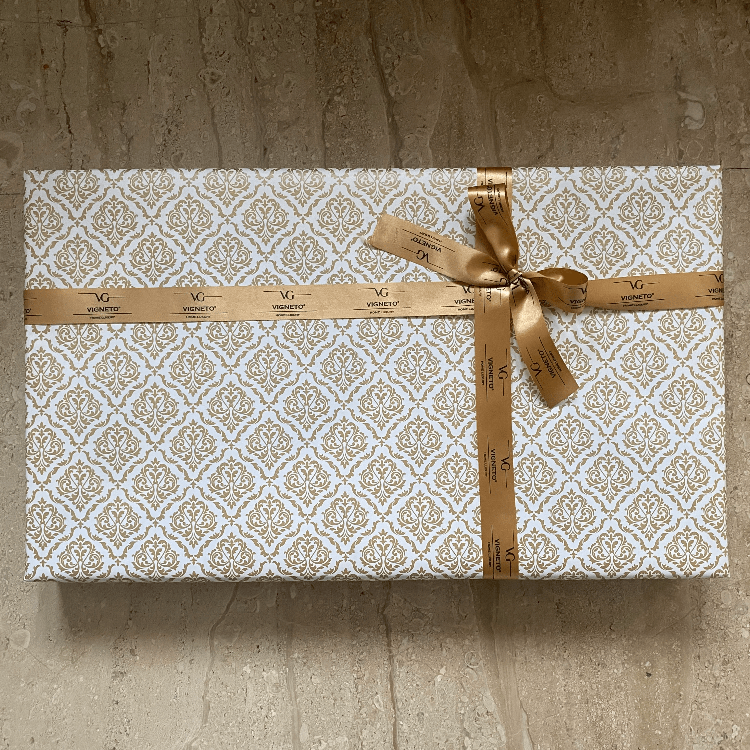 Gift box with decorative pattern and gold ribbon on a stone surface