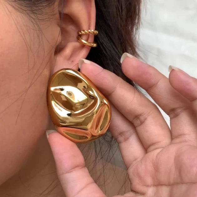 Gold earring for women being worn on a person's ear with a hand adjusting it.