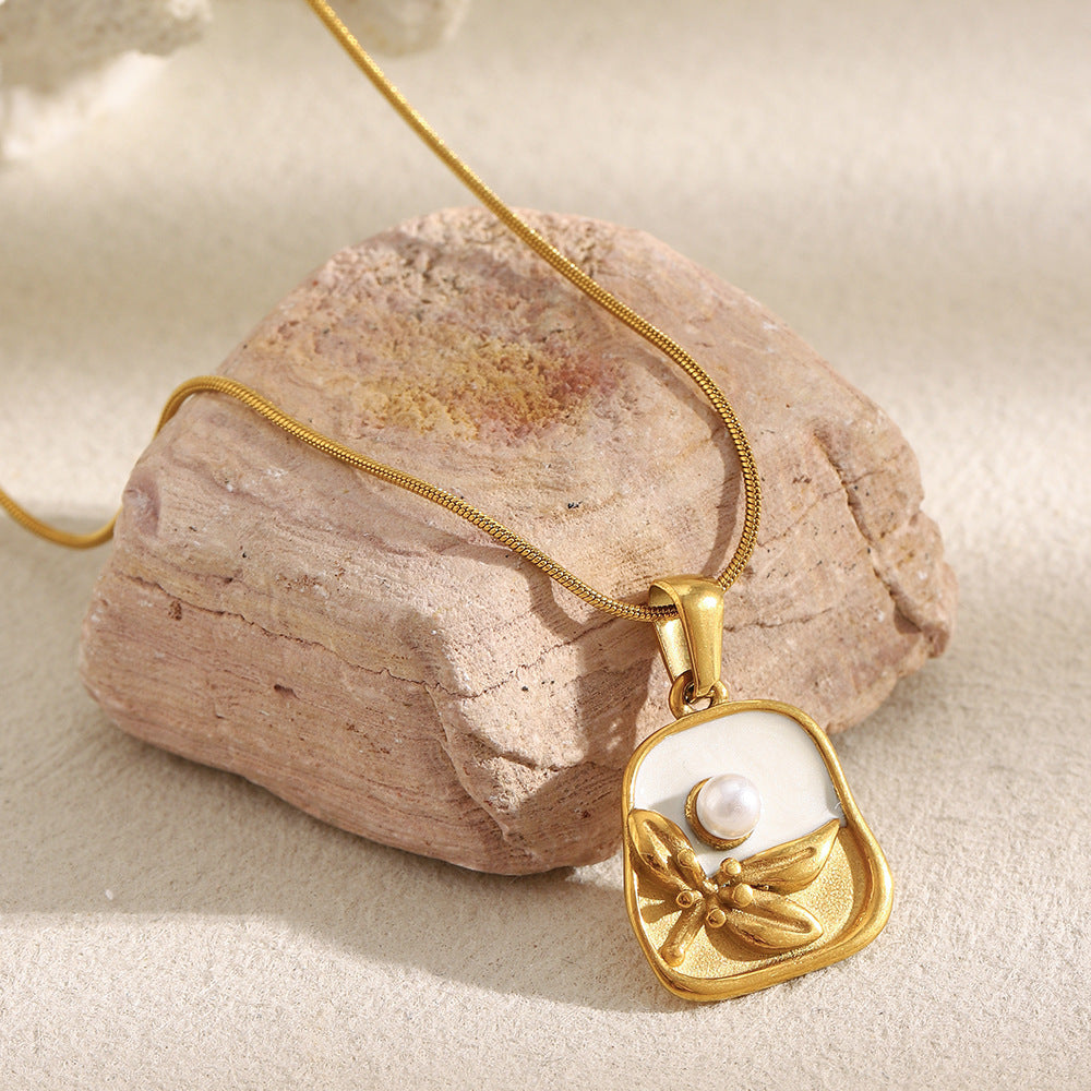 Gold necklace with a pendant fro women featuring a pearl and dragonfly design, resting on a rock.