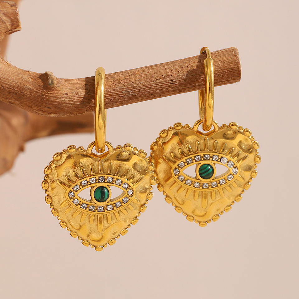 Gold heart-shaped earrings with eye design on a beige background