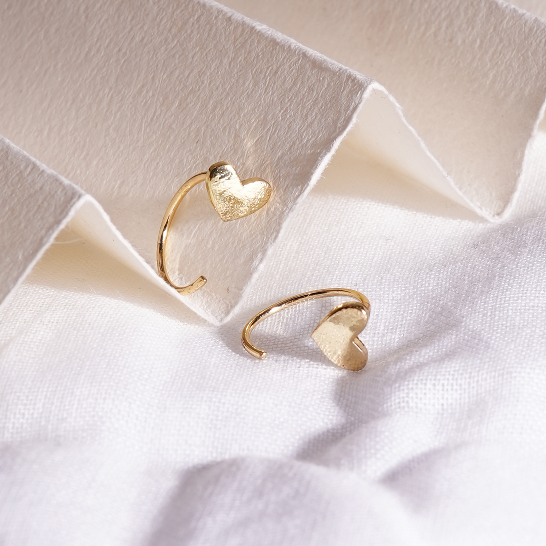 Gold heart-shaped earrings for women on a textured white fabric background