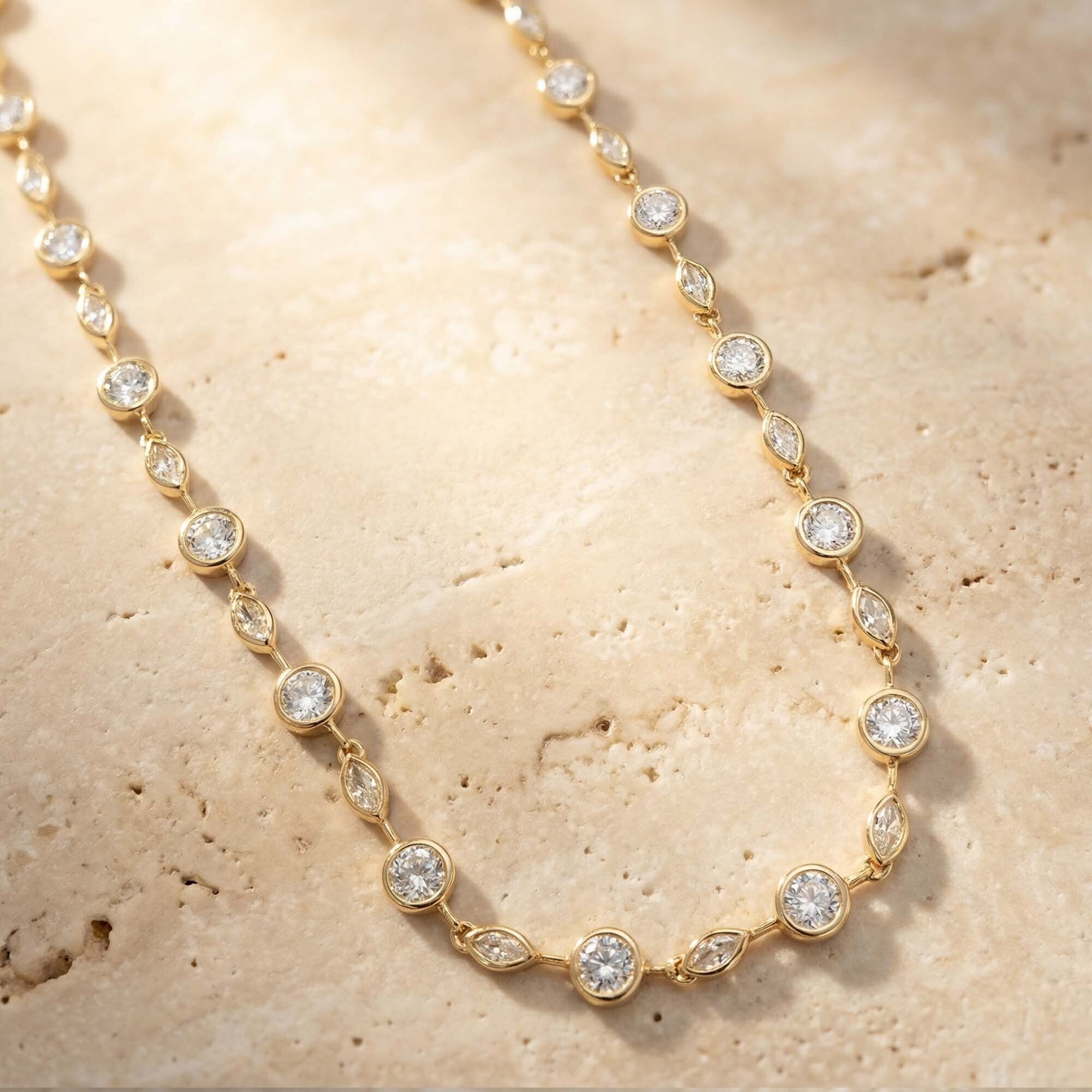 Gold necklace with clear stones on a beige stone surface