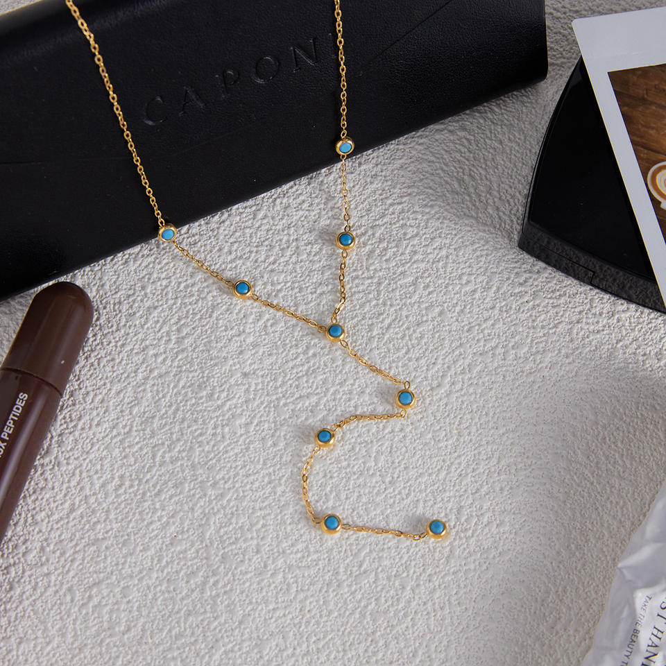 Gold necklace with blue stones on a textured surface next to a black box and brown tube.