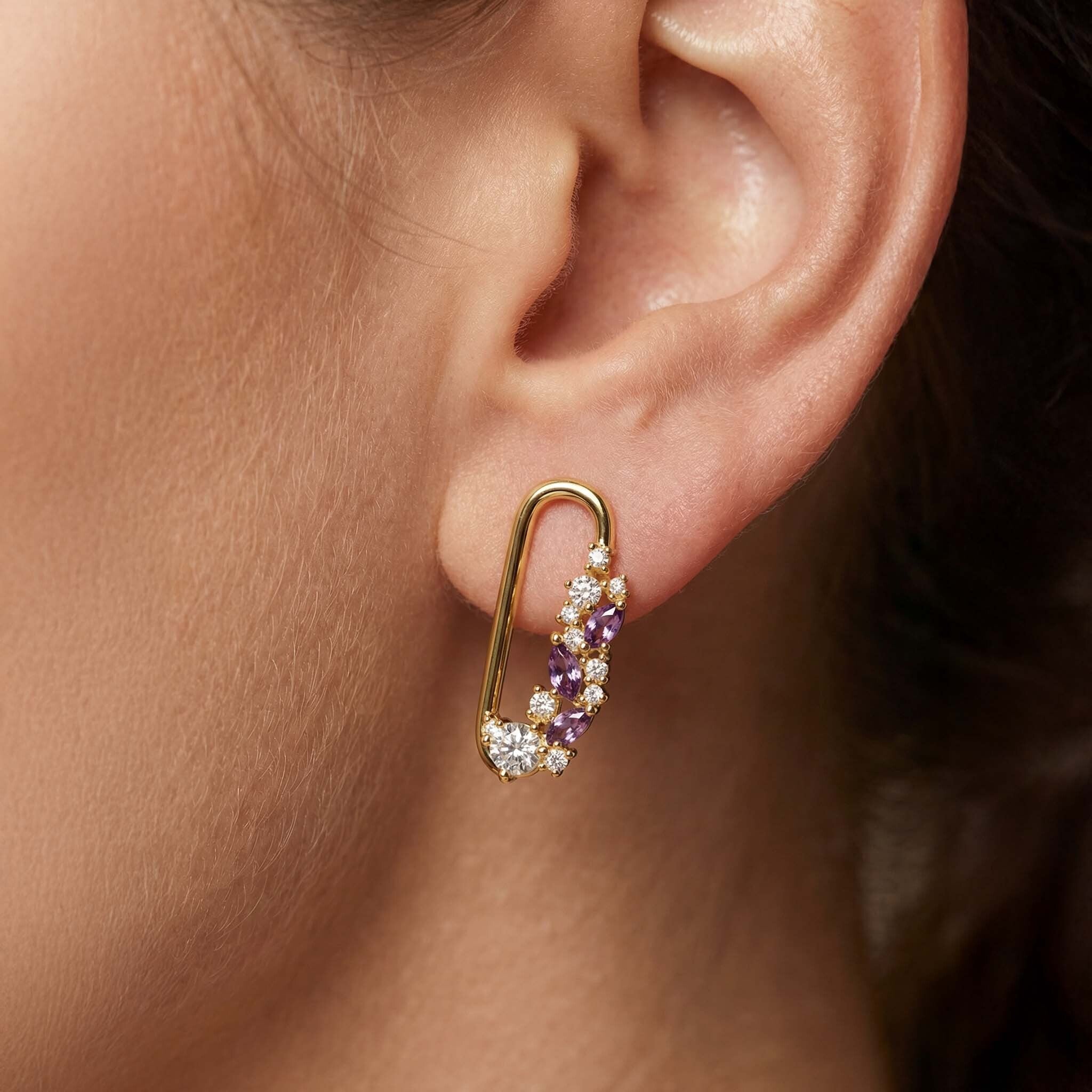 Gold earring with purple and white stones worn by a person