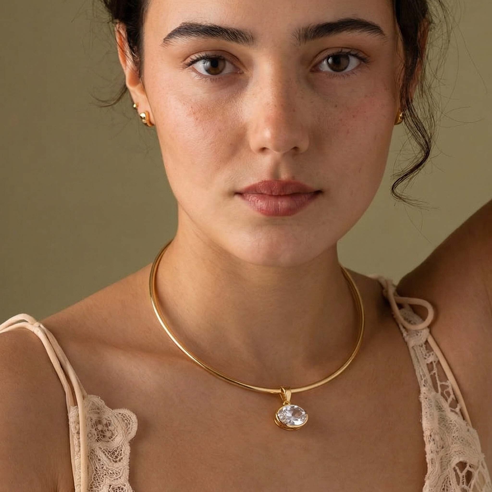 Woman wearing a gold necklace for women with a clear pendant against a neutral background