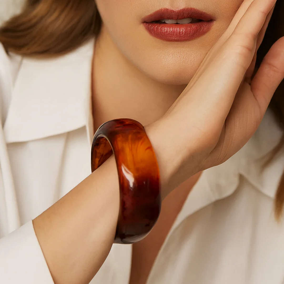 Close-up of a woman's hand wearing a large brown bangle with a blurred background