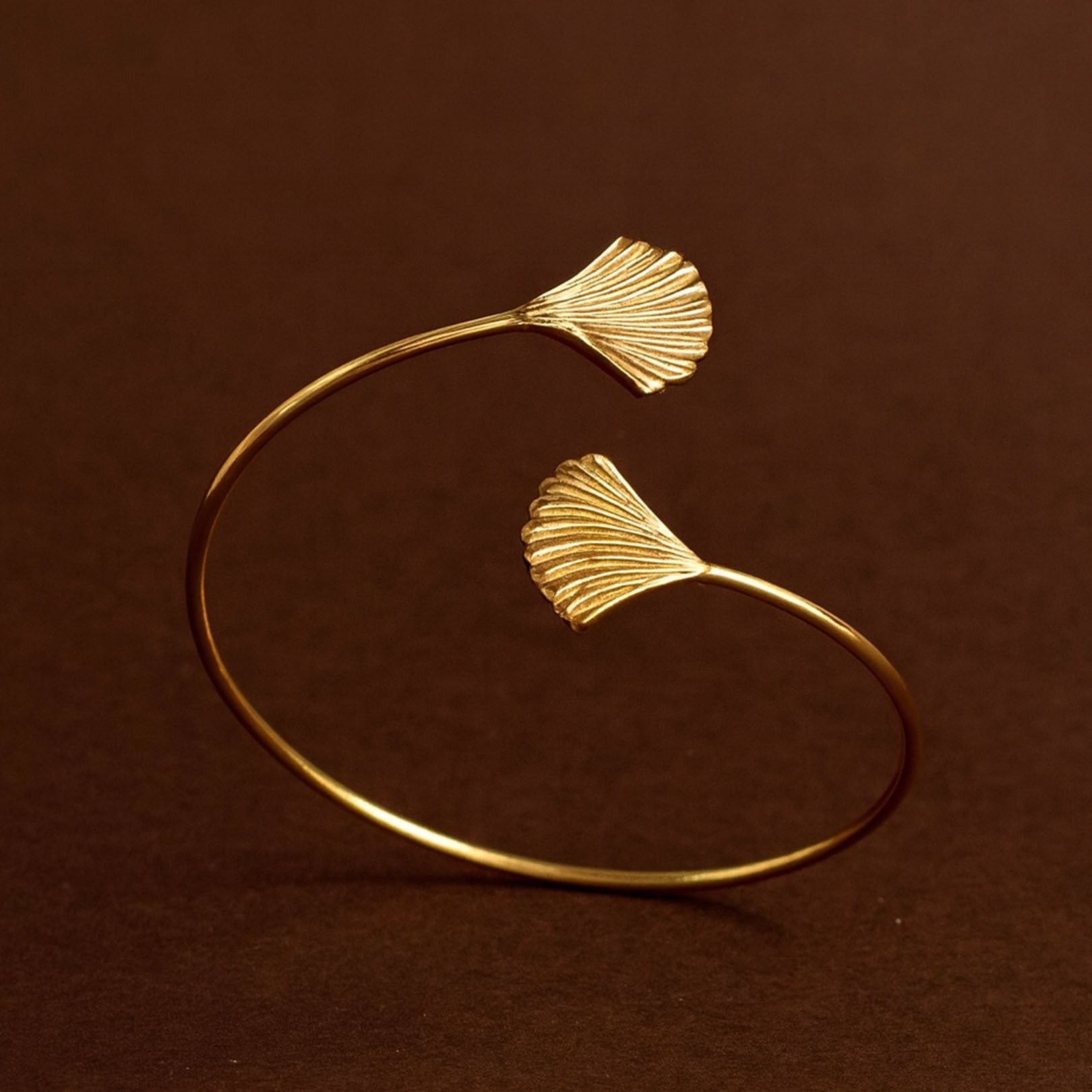 Gold bracelet with ginkgo leaf designs on a brown background