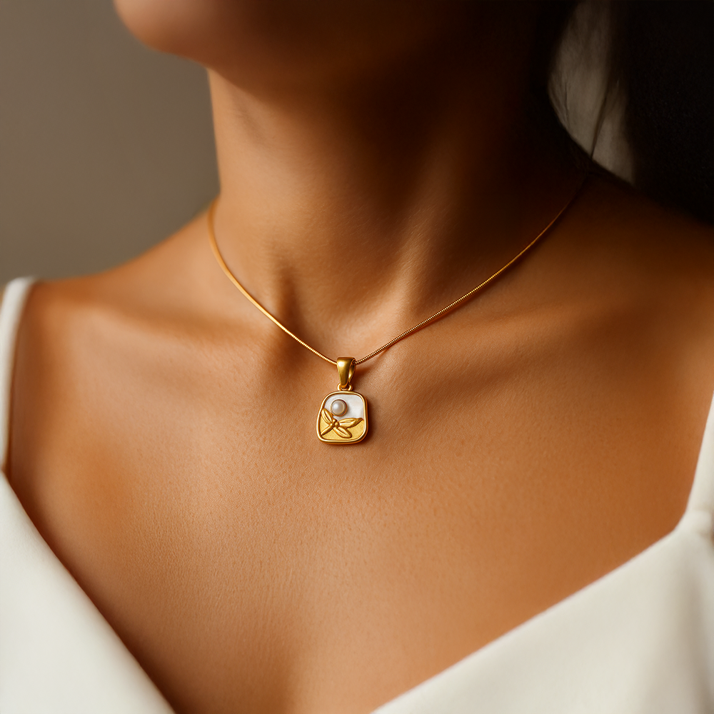 Gold necklace for women with a pendant on a person wearing a white top against a neutral background