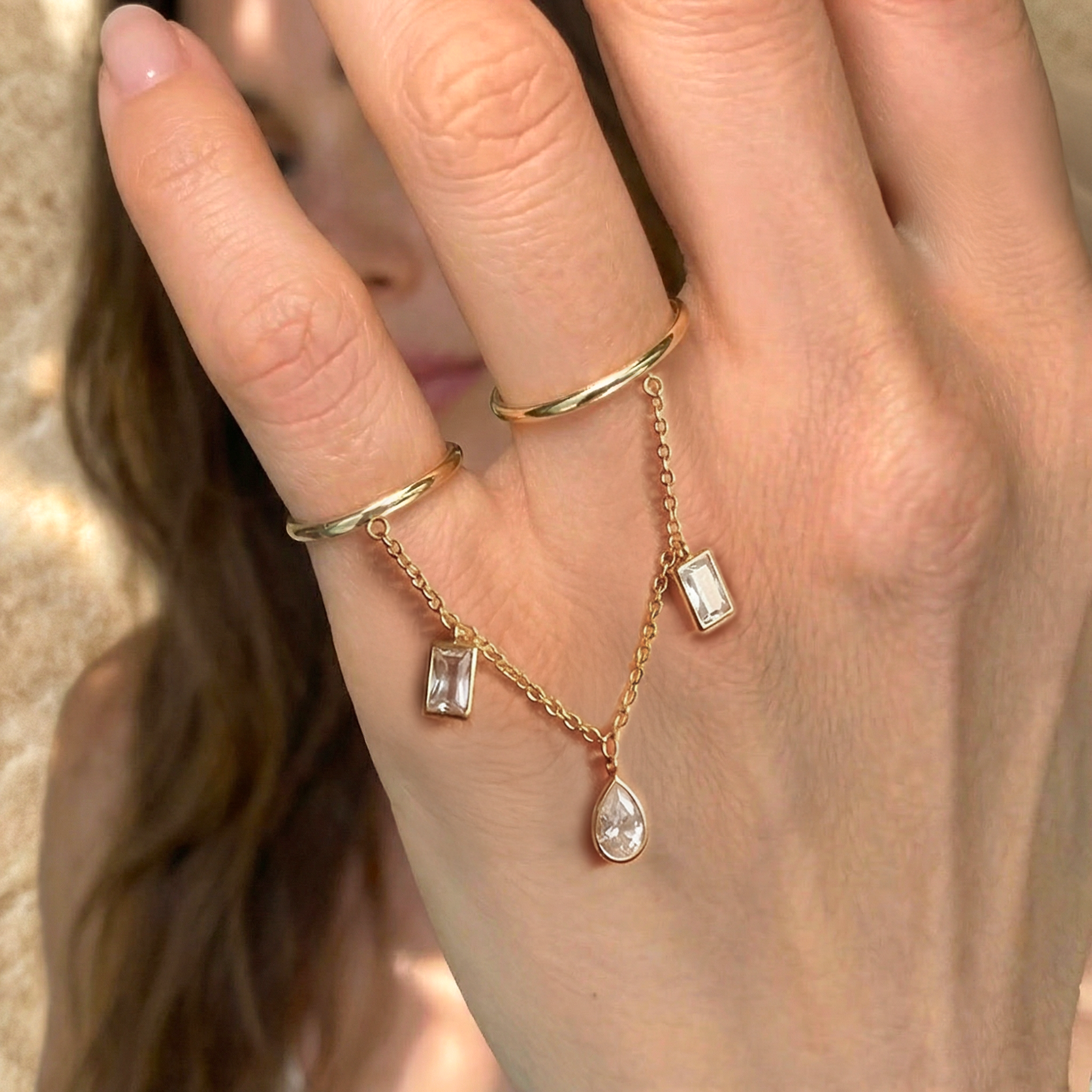 Gold ring with diamond pendants on a hand against a neutral background
