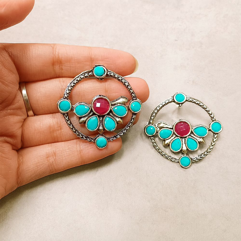 Silver earrings with turquoise and red stones held by a hand on a beige background