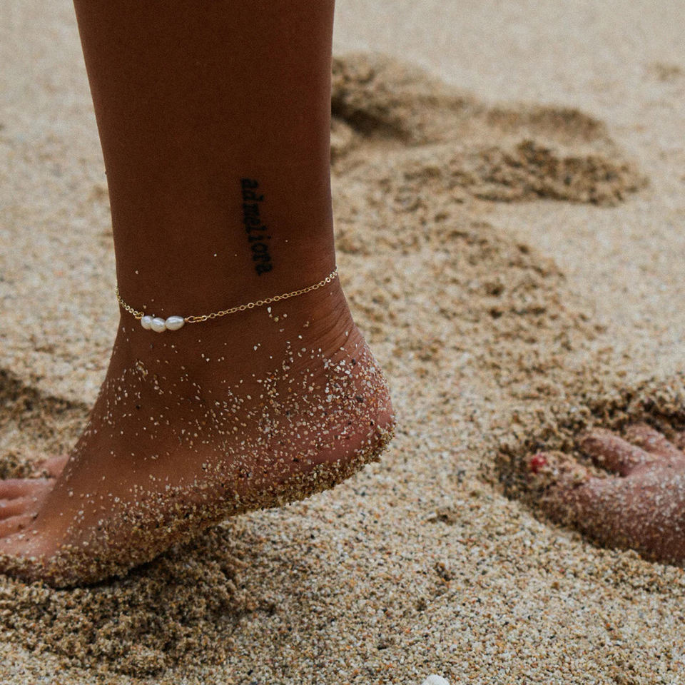 Person's ankle with a gold anklet on a sandy beach