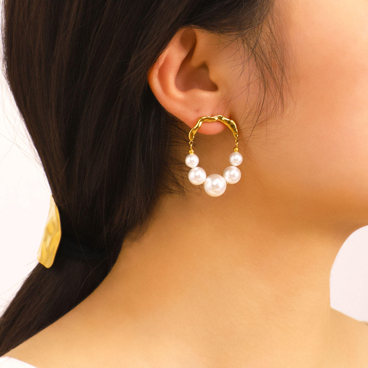 Close-up of a person wearing gold hoop earrings with pearl-like beads.