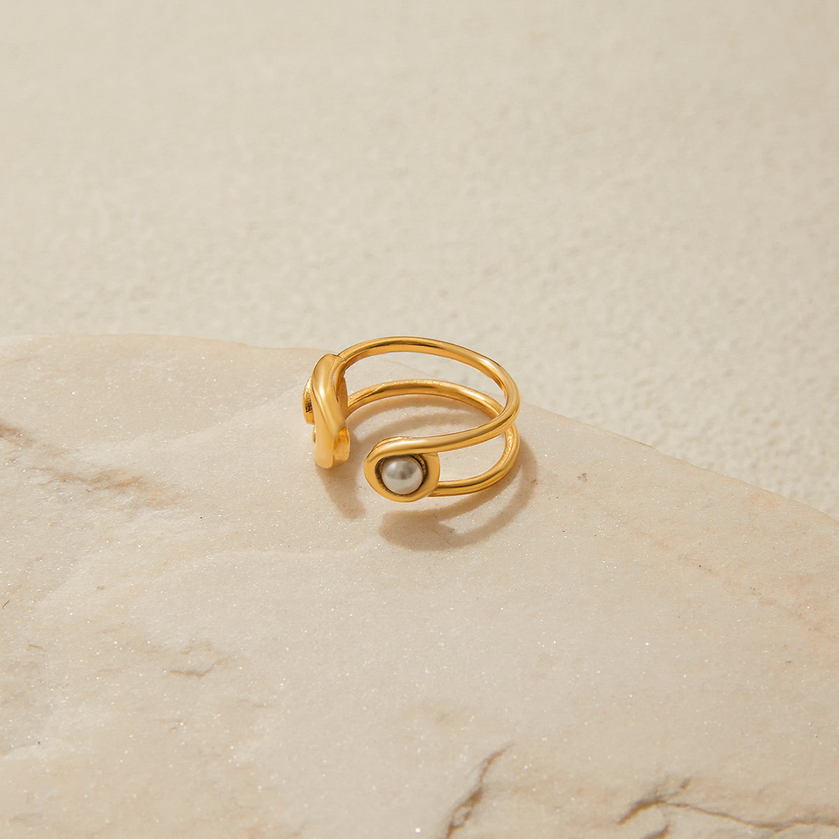 Gold ring with a pearl on a beige stone surface