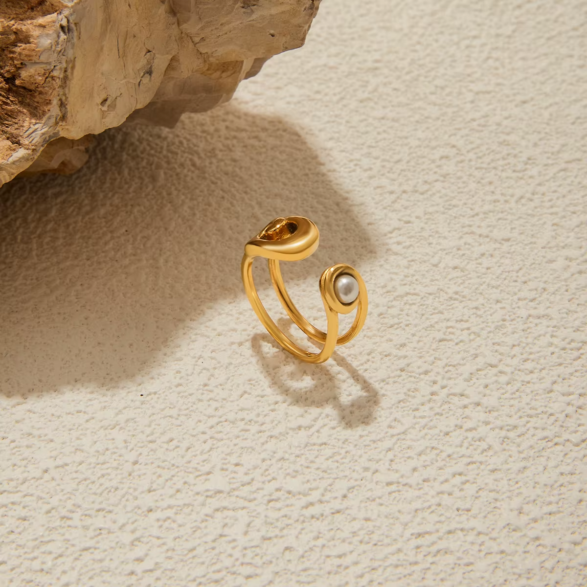 Gold ring with a pearl on a textured beige surface