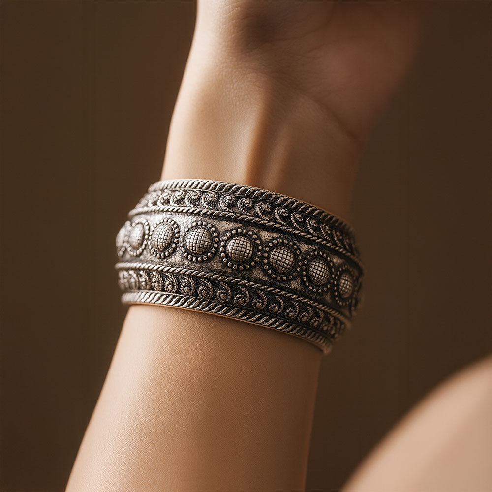 Close-up of a wrist wearing a detailed silver bracelet against a dark background