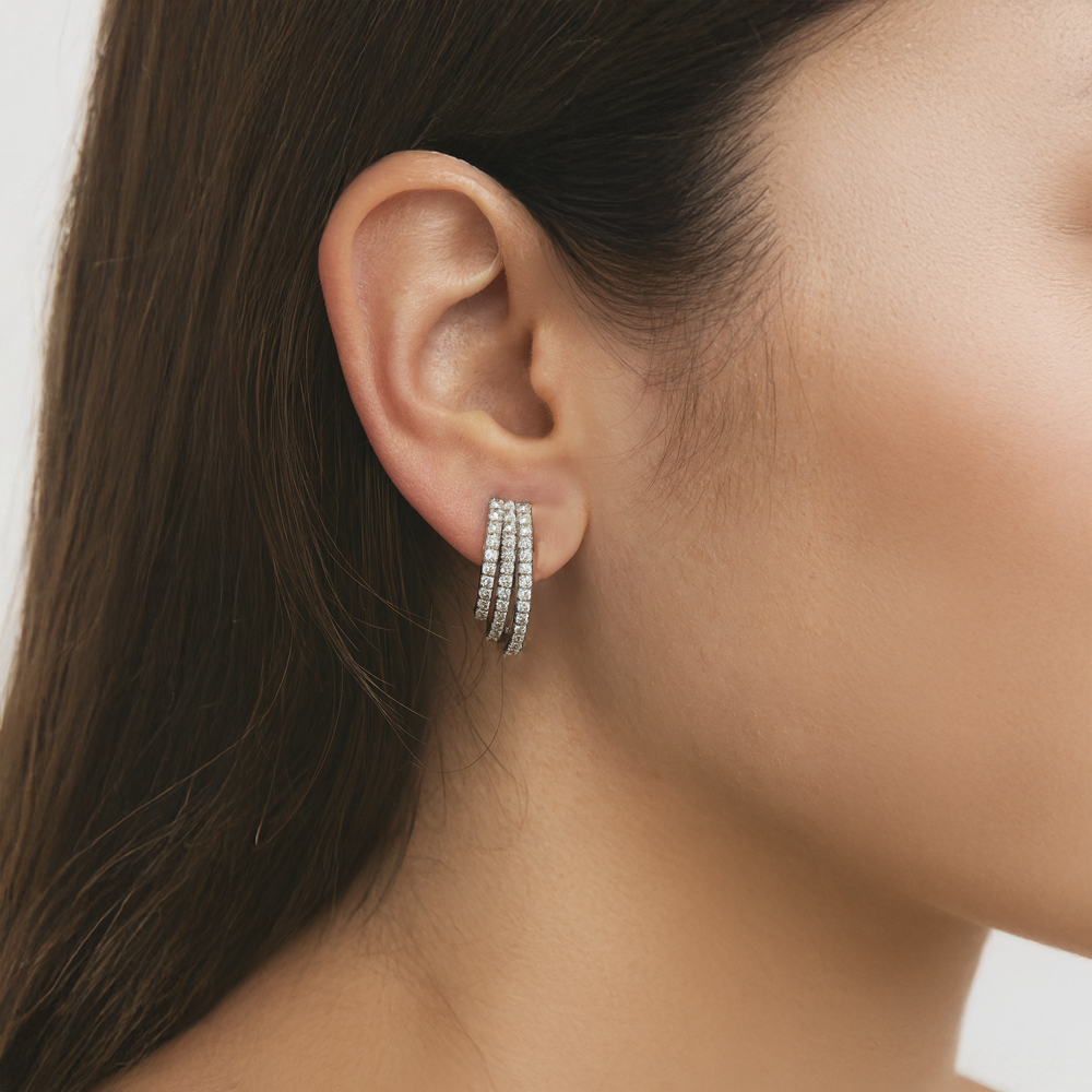Close-up of an ear wearing a silver hoop earring with a neutral background