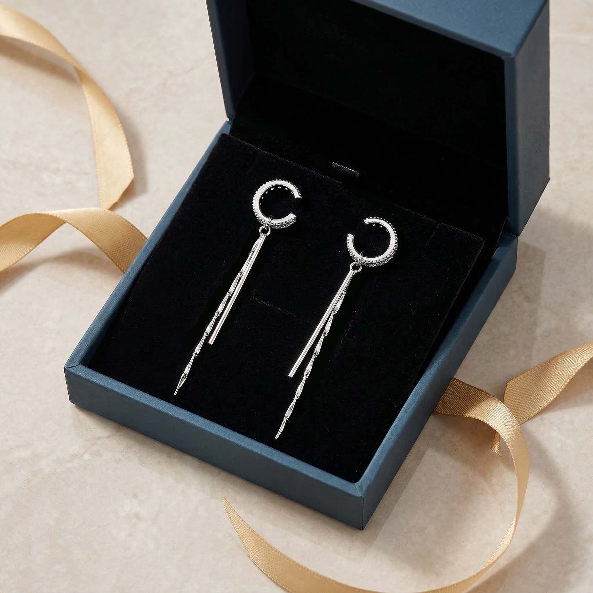 Silver earrings in an open jewelry box with a gold ribbon on a beige background gift for wife