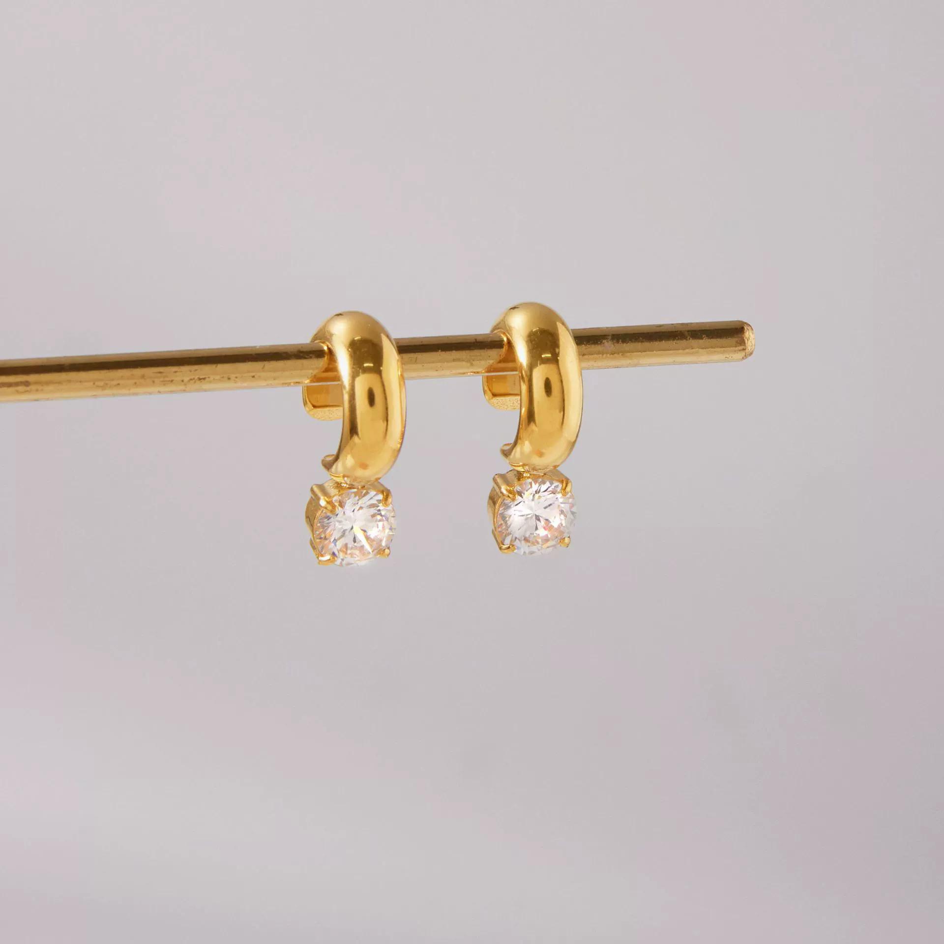 Gold hoop earrings with round gemstones on a gray background
