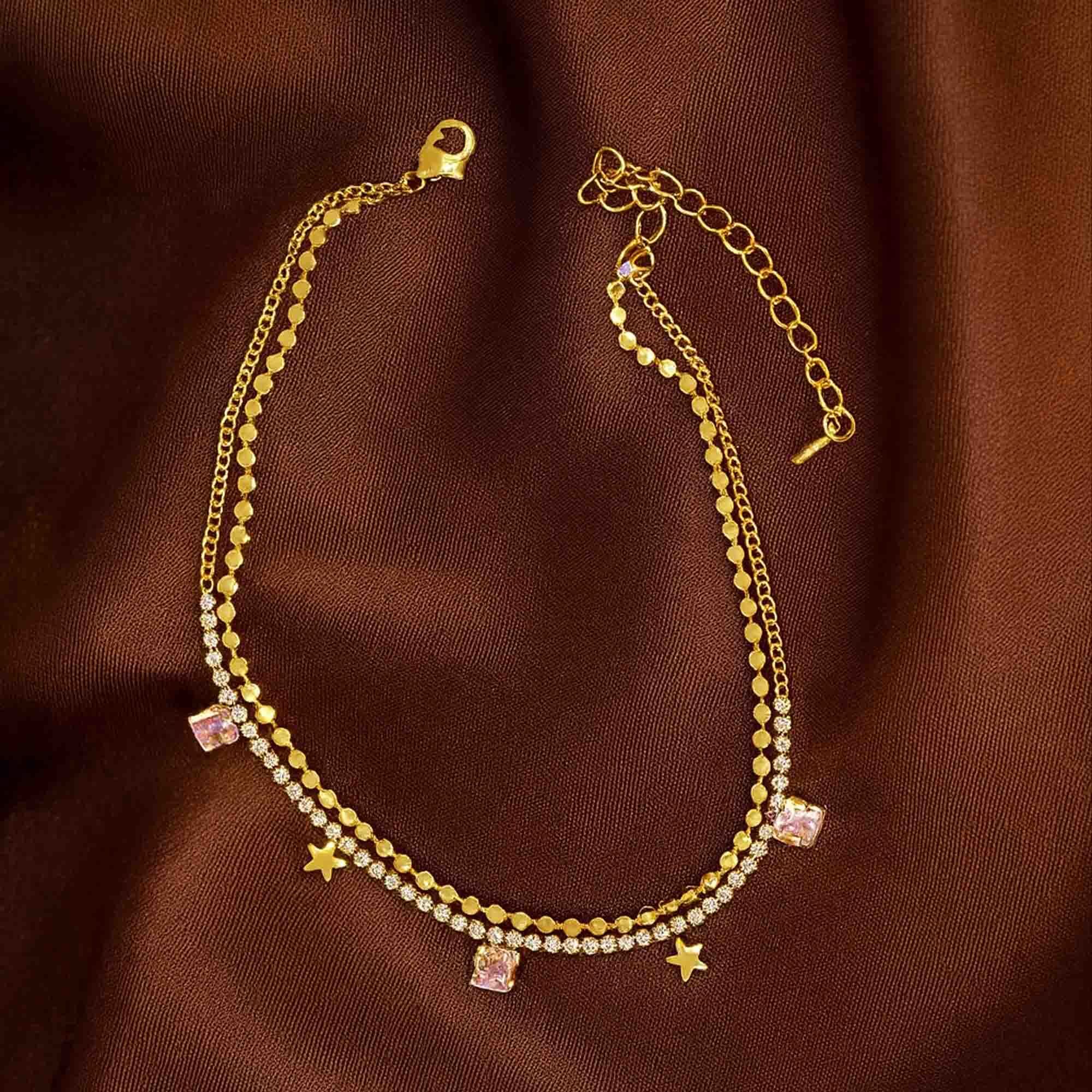 Gold anklets  with star and square charms on a brown fabric background