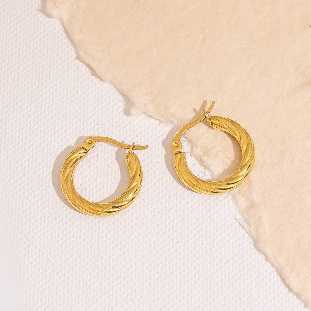 Gold hoop earrings for women on a textured beige and white background