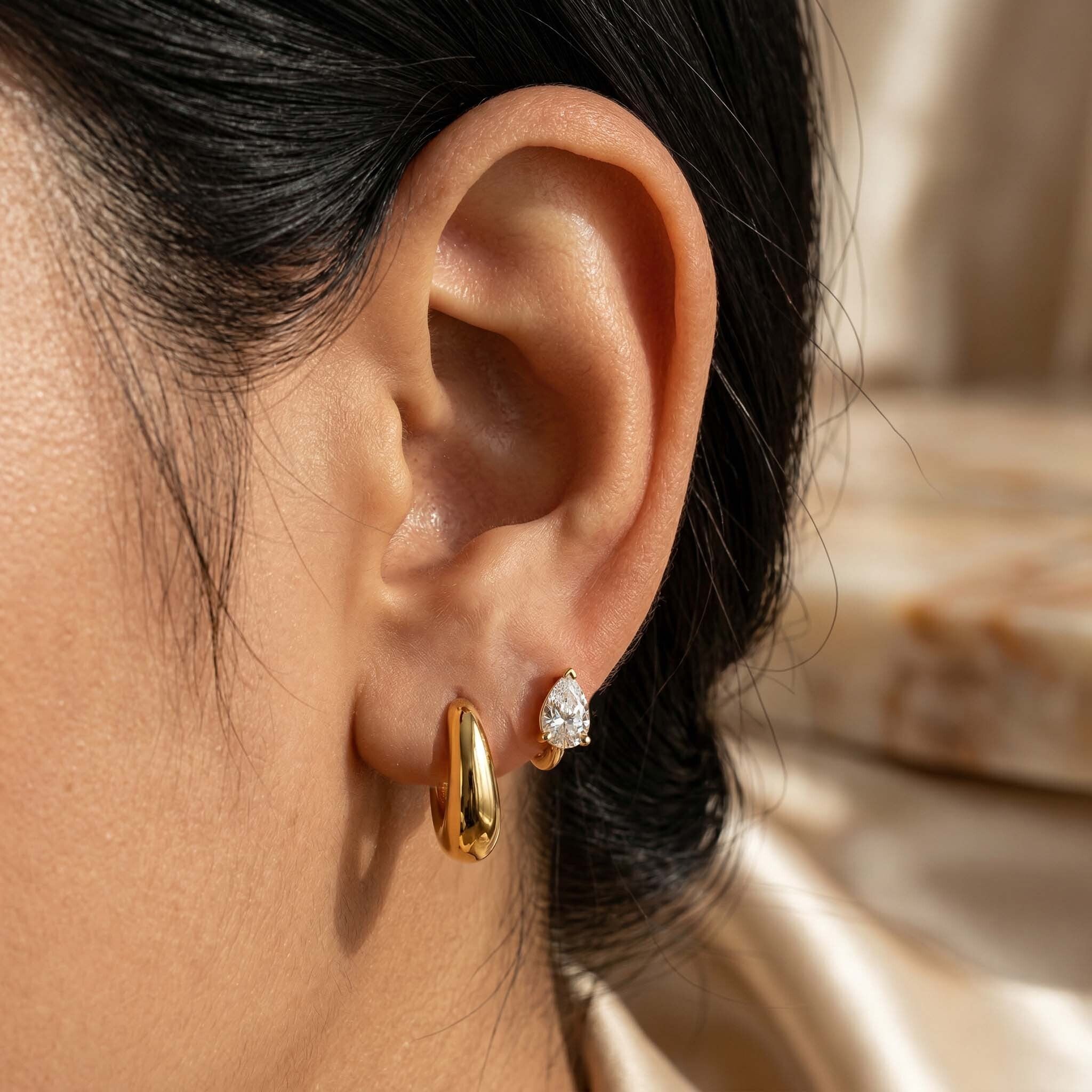 Close-up of an ear wearing gold hoop and diamond stud earrings.