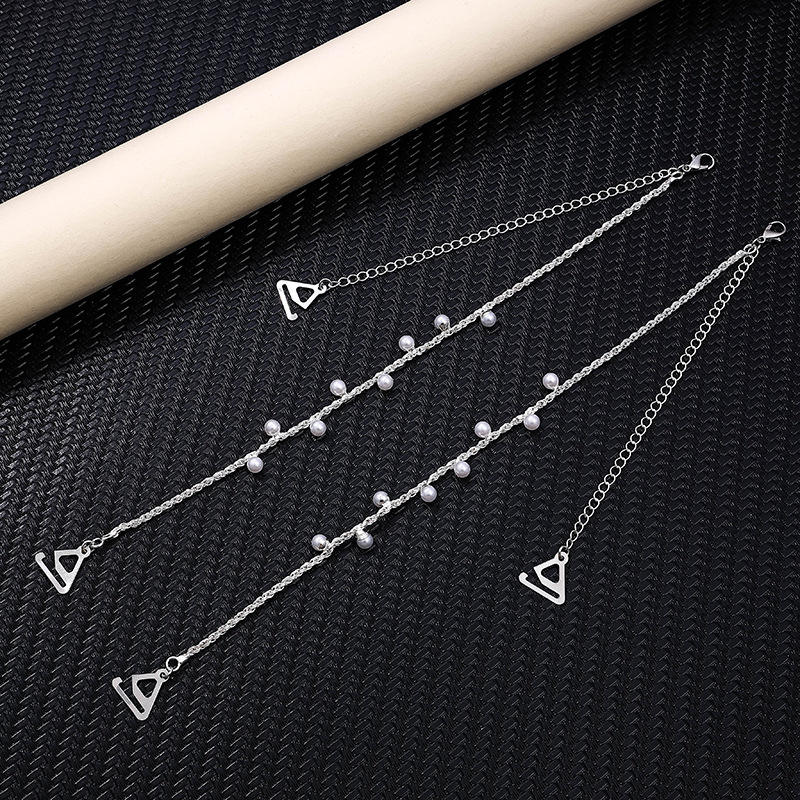 Three silver bra straap with triangle charms on a black textured surface.