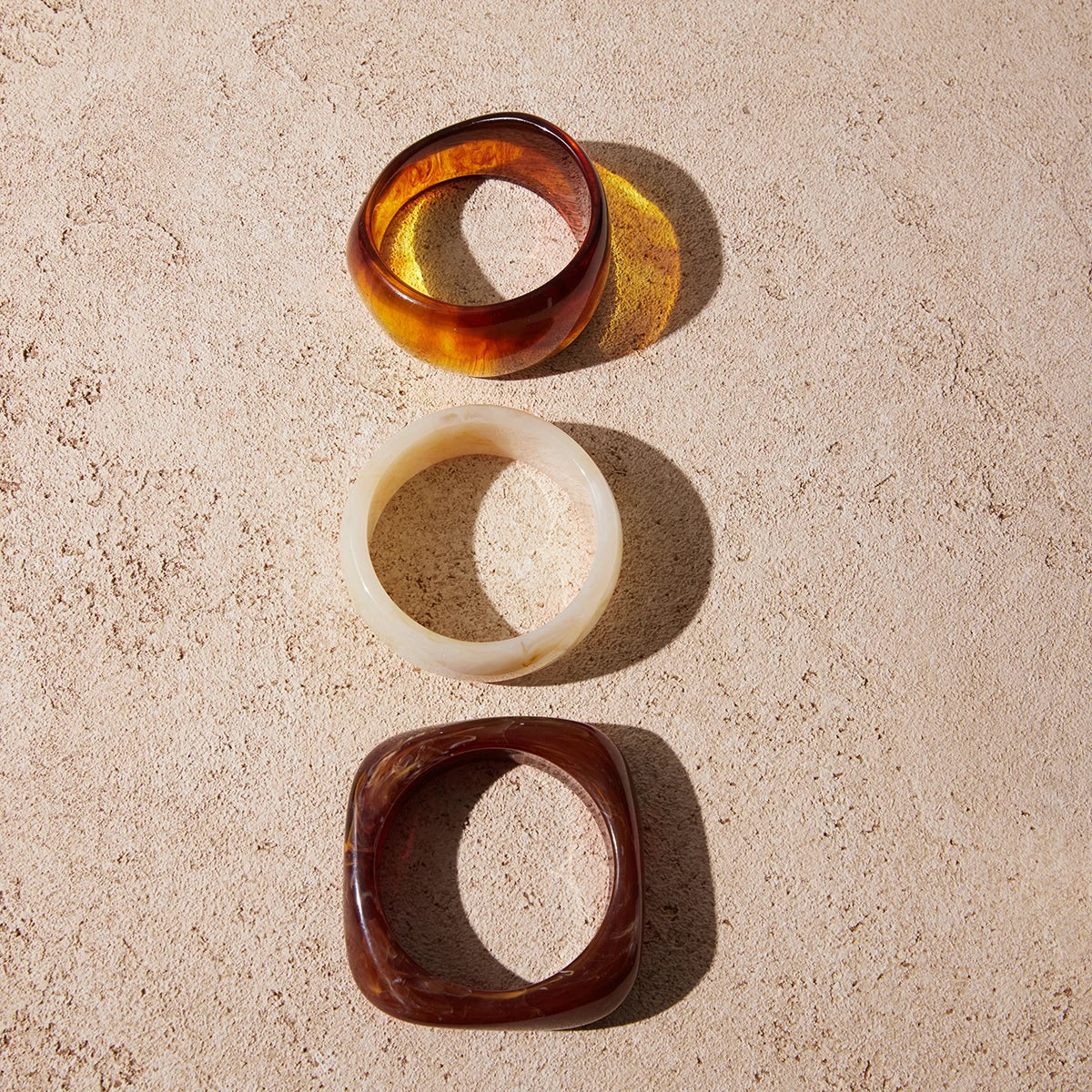 Three wooden Kada in different shapes and colors on a beige surface