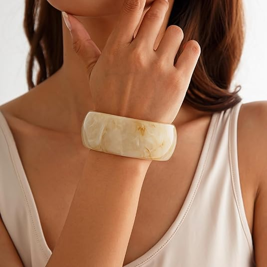 Woman wearing a large, light-colored stone bracelet on a plain background