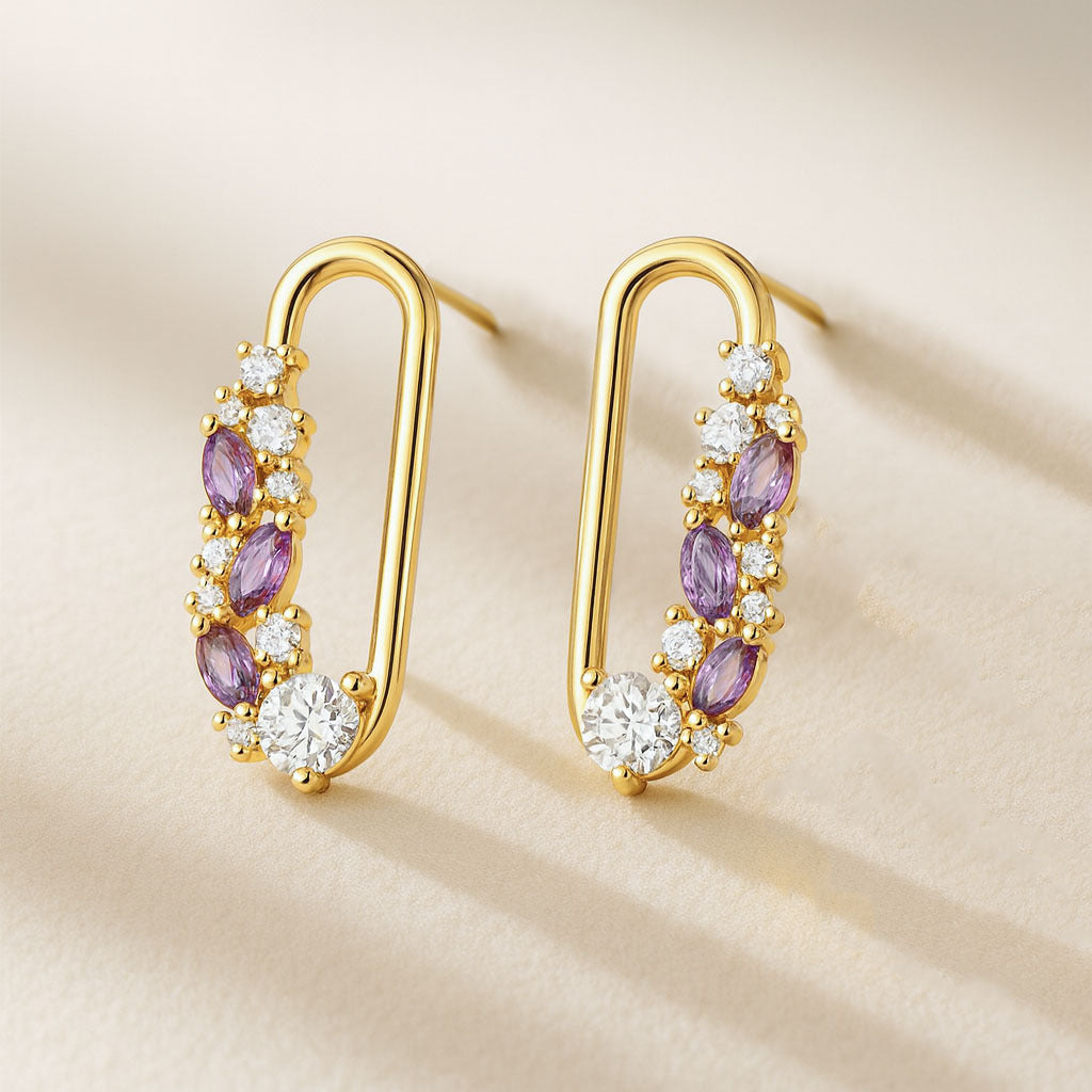 Gold hoop earrings with purple and clear gemstones on a beige background