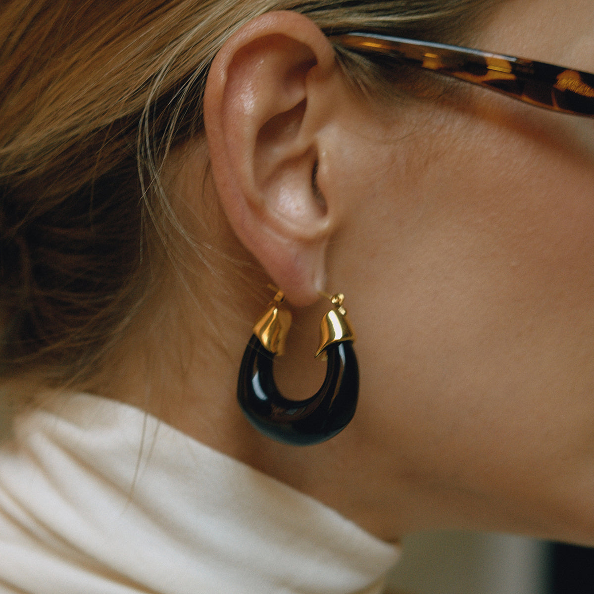 Close-up of an ear wearing a gold and black hoop earrings for women with a blurred background.