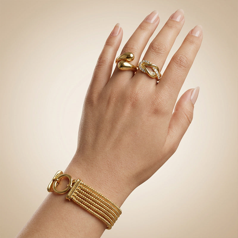 Hand wearing a gold bracelet and ring on a beige background